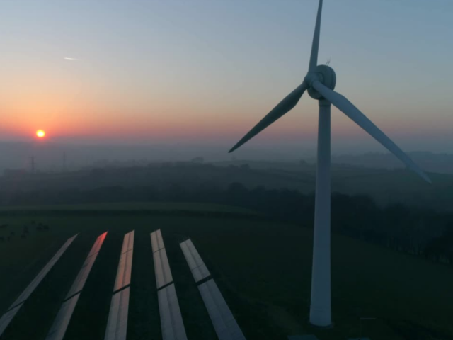 Windmill and solar panels against a sunset